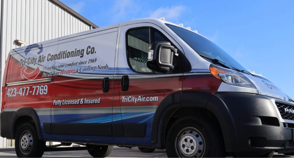 A TriCity Air Conditioning Co. service van parked outside a building, displaying company branding, contact number, and website on its side.
