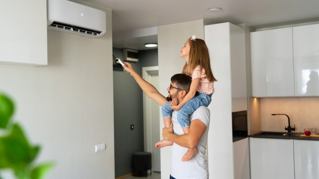 In a modern Windmere, TN home, a man carries a young girl on his shoulders as she uses a remote to turn on the air conditioner.