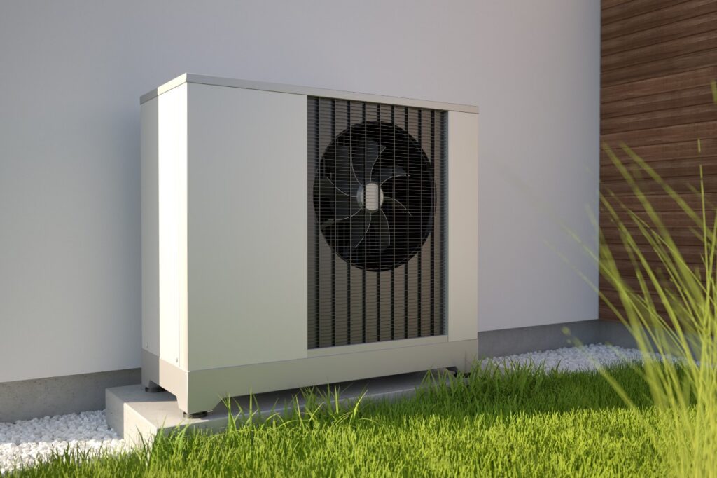 A modern outdoor heat pump unit sits on a concrete pad next to a building in Greene County, TN, surrounded by green grass and small white stones.